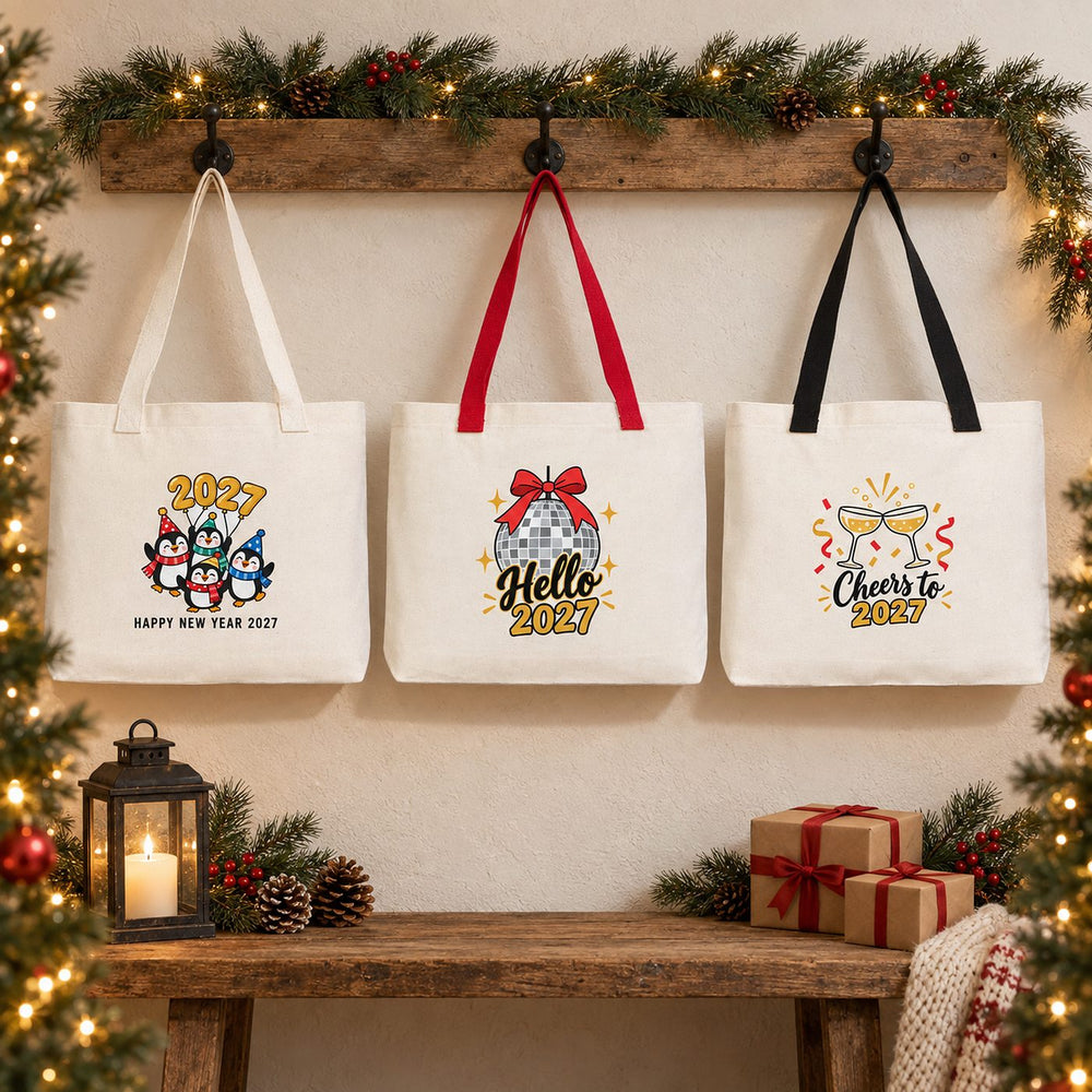 Three Christmas 2027 canvas tote bags with beige, red and black knitted straps hanging on a rustic wall with penguin, Hello 2027 disco ball and Cheers to 2027 prints