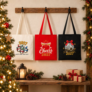 Three Christmas 2027 cotton gabardine tote bags in natural, red and black hanging side by side on a rustic wall with penguin, Cheers 2027 and Hello 2027 prints