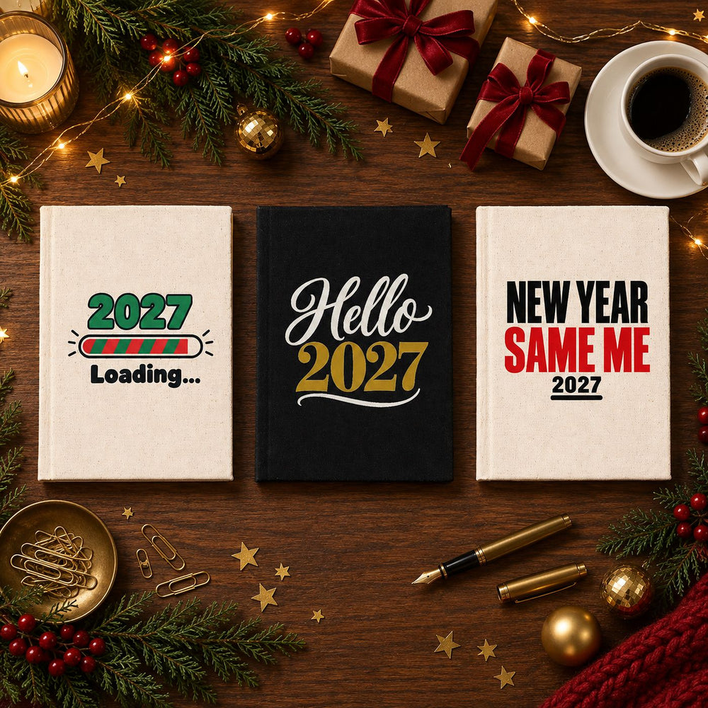 Three Christmas and New Year 2027 canvas notebooks, natural and black, with 2027 Loading, Hello 2027 and New Year Same Me prints on a festive planning desk