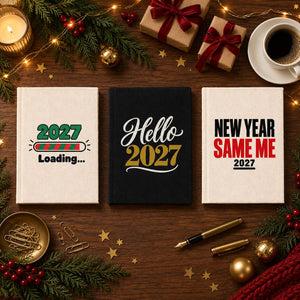 Three Christmas and New Year 2027 canvas notebooks, natural and black, with 2027 Loading, Hello 2027 and New Year Same Me prints on a festive planning desk