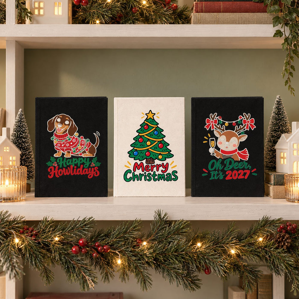 Three Christmas and New Year 2027 canvas notebooks, natural and black, with 2027 Loading, Hello 2027 and New Year Same Me prints on a festive planning desk
