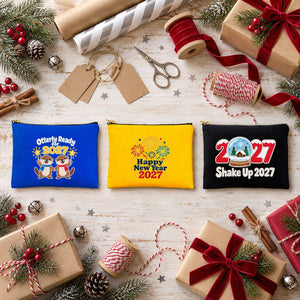 Three printed cotton clutch bags, royal blue, yellow and black, with Otterly Ready for 2027, Happy New Year 2027 fireworks and Shake Up 2027 snow globe prints on a gift-wrapping table
