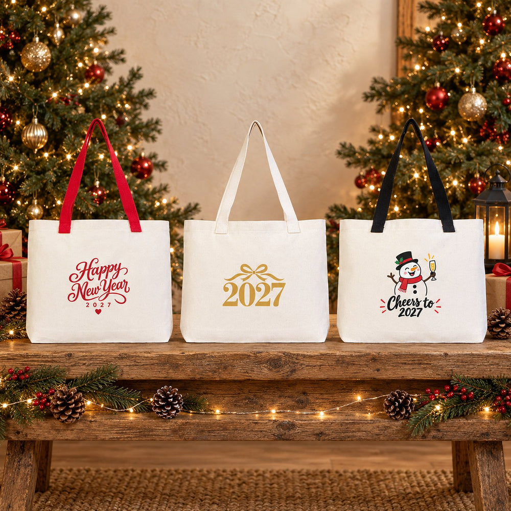Three Christmas 2027 canvas tote bags with beige, red and black knitted straps hanging on a rustic wall with penguin, Hello 2027 disco ball and Cheers to 2027 prints