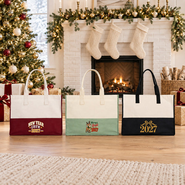 Burgundy, sage green and black canvas tote bags with New Year Crew 2027, Merry and Bright reindeer and gold 2027 bow prints in front of a white brick fireplace with stockings