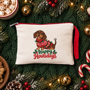Cream clutch with a red zipper and a Happy Howlidays dachshund print on a green knit blanket with hot cocoa, dog biscuits and candy canes