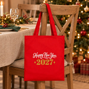 Red cotton gabardine tote bag with an ivory and gold Happy New Year 2027 print hanging on a chair at a Christmas table