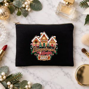 Black clutch makeup bag with a Gingerbread Village 2027 print on a marble vanity with perfume, lipstick, makeup brushes and gold ornaments