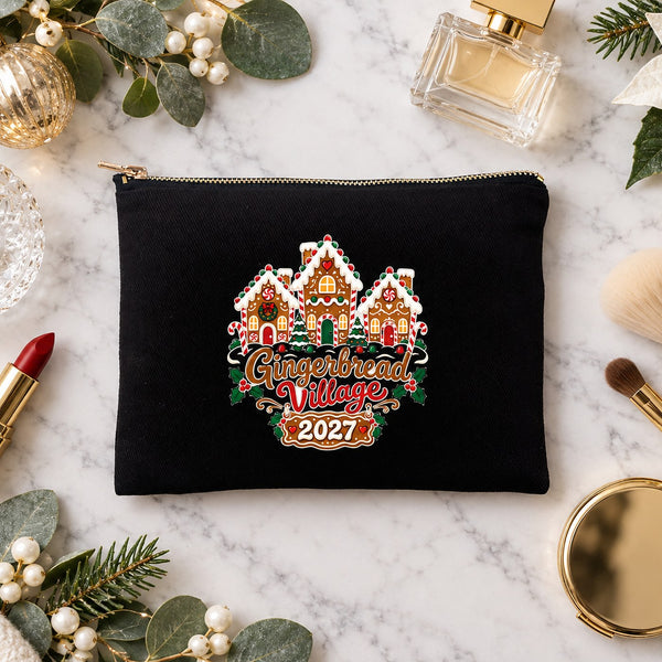 Black clutch makeup bag with a Gingerbread Village 2027 print on a marble vanity with perfume, lipstick, makeup brushes and gold ornaments
