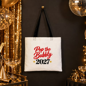 Cotton tote bag with black handles and a Pop the Bubbly 2027 print hanging at a gold New Year's Eve party with champagne