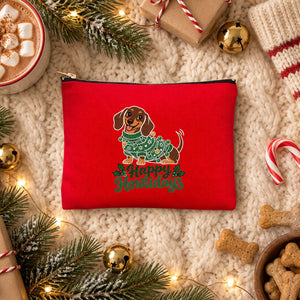 Red clutch bag with a Happy Howlidays dachshund print on a cream knit blanket with hot cocoa, a striped stocking, candy canes and dog treats