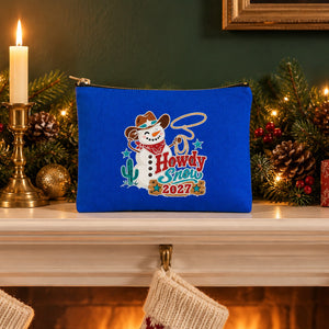 Royal blue clutch bag with a Howdy Snow 2027 cowboy snowman print standing on a Christmas fireplace mantel with a garland, candles and stockings