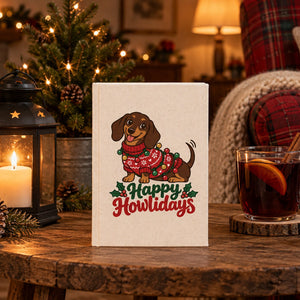 Natural canvas notebook with a Happy Howlidays dachshund print standing on a rustic side table by a lantern and mulled wine on Christmas evening