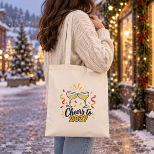 Natural cotton gabardine tote bag with a Cheers to 2027 champagne print carried on the shoulder in a snowy Christmas street