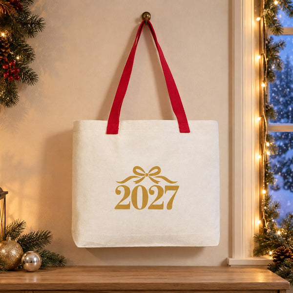 Large canvas tote bag with red knitted straps and a gold bow 2027 print hanging by a snowy window