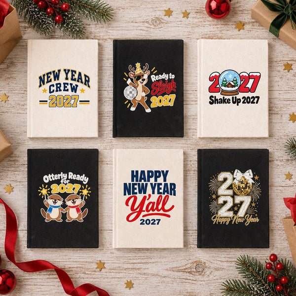 Six canvas notebooks in natural and black with different Christmas and New Year 2027 designs laid out as bulk holiday gifts for a team