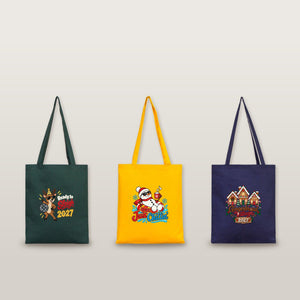 Studio photo of three cotton gabardine tote bags in green, yellow and navy with Ready to Sleigh 2027, Just Chillin' 2027 and Gingerbread Village 2027 prints
