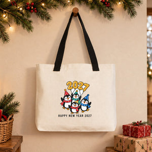 Large canvas tote bag with black knitted straps and a party penguins Happy New Year 2027 print hanging on a wooden peg in a Christmas entryway