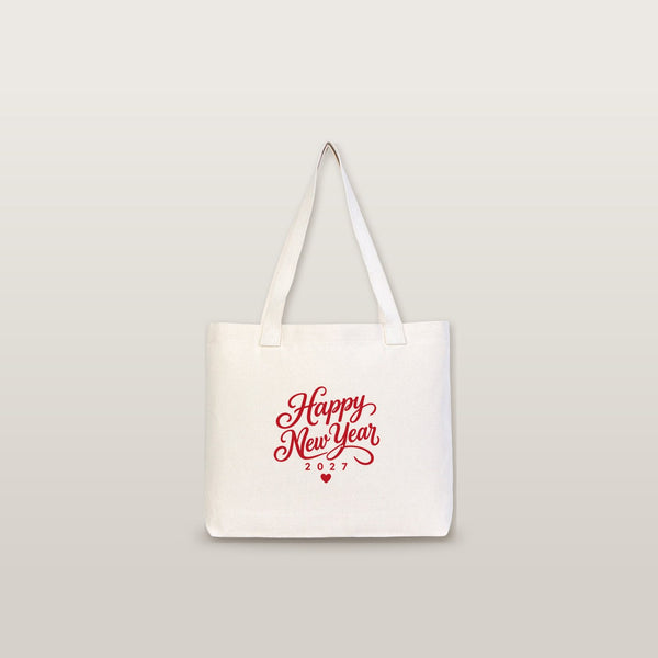 Studio photo of a large canvas tote bag with beige knitted straps and a red Happy New Year 2027 script print