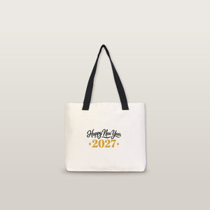 Studio photo of a large canvas tote bag with black knitted straps and a Happy New Year 2027 gold print
