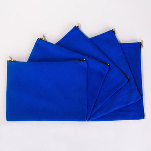 Real photo of five royal blue cotton clutch bags fanned out, showing the flat pouch and brass zippers