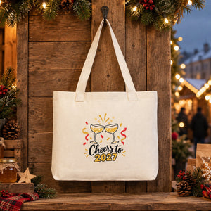 Large canvas tote bag with beige knitted straps and a Cheers to 2027 champagne print hanging at a Christmas market stall
