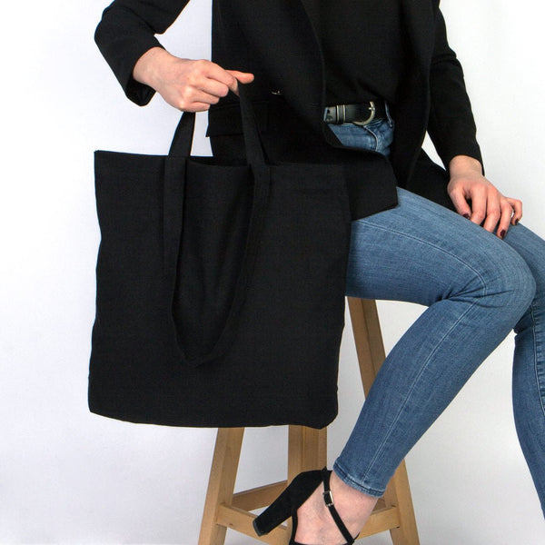 Person holding a black tote bag with a white background