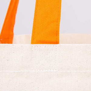 Close-up of a white woven bag with orange handles on a light gray background
