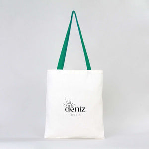 White tote bag with green straps and 'deniz butik' logo on a light gray background