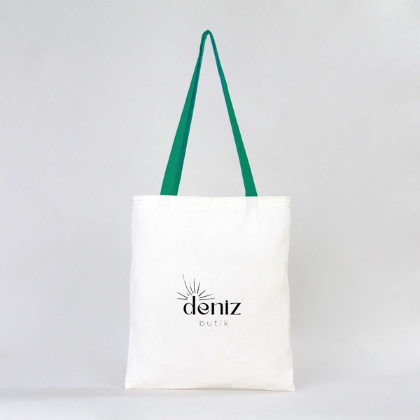 White tote bag with green straps and 'deniz butik' logo on a light gray background