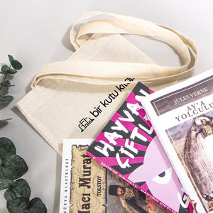 Beige tote bag with books and a plant on a light background