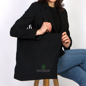 Person holding a black tote bag with 'techbox' logo against a white background