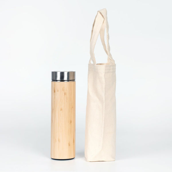 Bamboo water bottle with a metal cap next to a beige tote bag on a white background