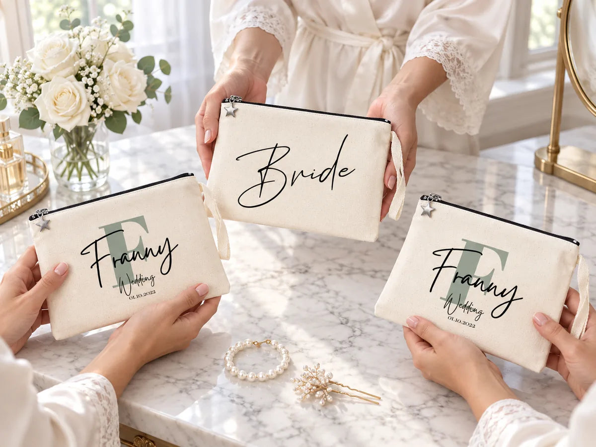 Handen van bruidsmeisjes in zijden ochtendjassen aan een marmeren kaptafel, met een clutch ‘Bride’ en twee clutches ‘Franny Wedding’, witte rozen en een parelarmband